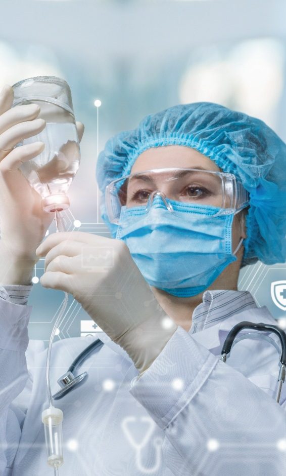 Infusionsvorbereitung Ärztin bereitet in Schutzkleidung das System für Infusionen vor, während im Hintergrund ein verschwommenes Bild zu sehen ist